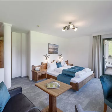Comfort meets nature: The spacious double room "Wilder Kaiser" with stylish furnishings, a cozy seating area, and a balcony with views of the Tyrolean Alps.