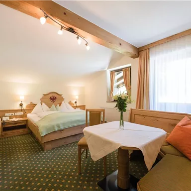 Ein gemütliches Hotelzimmer mit zwei Betten und einem Tisch. Die Fenster sind hell, und ein Blumenstrauß schmückt den Tisch.