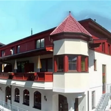 A charming building in alpine style with red and white elements. The facade has many windows and an attractive balcony.