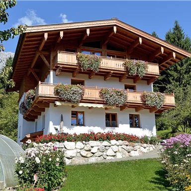 A charming wooden house with a balcony and flower boxes. Surrounded by a well-maintained garden and trees.