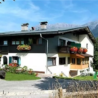 A cozy vacation home with flower-filled balconies and a beautiful landscape in the background. The surroundings are green and invite relaxation.