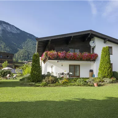 A cozy house with a well-kept garden and colorful flowers. In the background, the mountains can be seen, creating a picturesque alpine landscape.