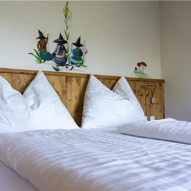 Ein gemütliches Schlafzimmer mit einem Holzbett und zwei weißen Kopfkissen. An der Wand ist eine dekorative Malerei zu sehen.