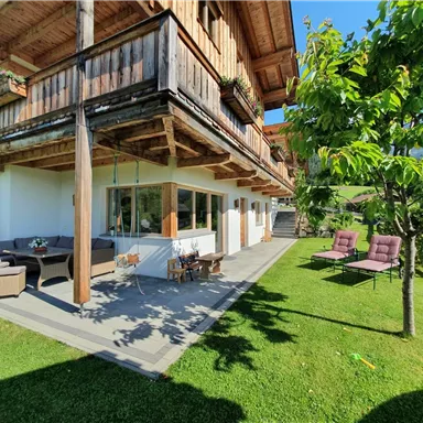 A cozy holiday home with wood paneling and a beautiful garden. There are comfortable seating areas and plenty of sunlight.