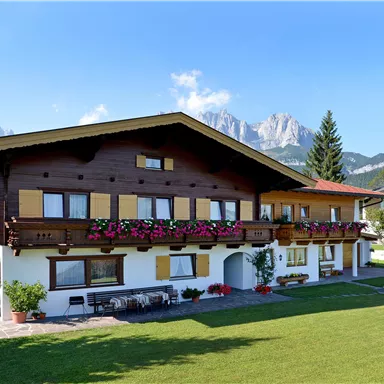 Ein schönes Holzhaus mit Balkon und bunten Blumen. Im Hintergrund sind majestätische Berge und ein klarer Himmel zu sehen.