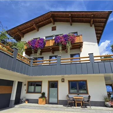 Ein modernes Haus mit einem schönen Balkon, der mit blühenden Pflanzen dekoriert ist. Der klare Himmel ergänzt die einladende Atmosphäre.