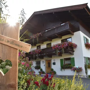 Ein charmantes Haus mit einem herzlichen Willkommen-Schild aus Holz. Bunte Blumen schmücken die Fenster und den Garten.