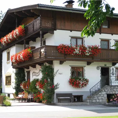 Ein hübsches, traditionelles Haus mit Blumenkästen und Holzverzierungen. Es ist von einem gepflegten Garten umgeben.