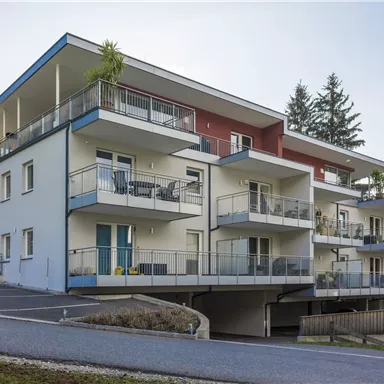 A modern residential building with several balconies and a bright facade. Surrounded by trees and a peaceful environment.