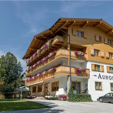 Ein charmantes Holzgebäude mit Balkonen und bunten Blumen. Umgeben von viel Grün in einer ruhigen Umgebung.
