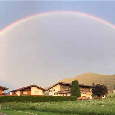 Ein schöner Regenbogen spannt sich über malerische Häuser und grüne Wiesen. Die Landschaft ist friedlich und lädt zum Staunen ein.