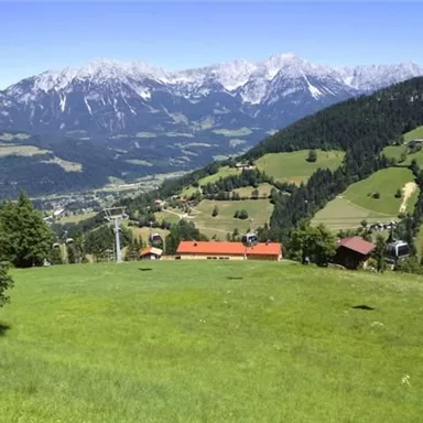 A picturesque landscape with gentle green hills and snow-capped mountains in the background. The scene also features some houses and a cable car.