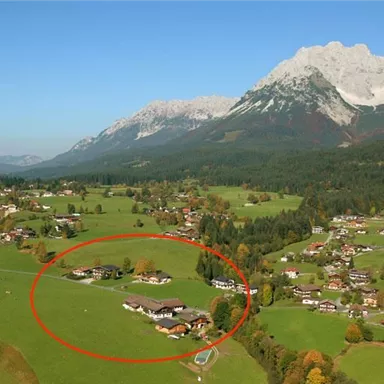 Eine malerische Landschaft mit grünen Wiesen und verstreuten Häusern. Im Hintergrund sind majestätische Berge zu sehen, die den Himmel berühren.