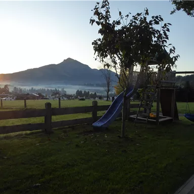 A beautiful garden with a slide and a playground. Mountains and a sunrise are visible in the background.
