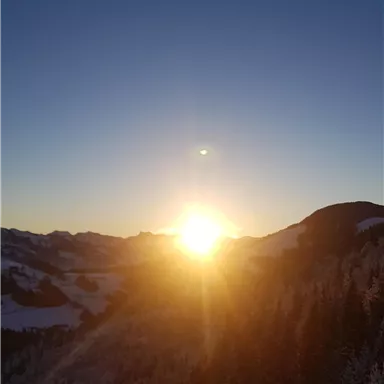 A stunning view of a sunrise over the snow-covered mountains. The sun radiates over the landscape, creating a warm, golden atmosphere.