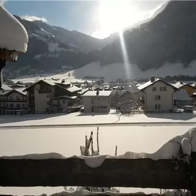 Eine verschneite Landschaft mit Häusern und Bergen im Hintergrund. Die Sonne scheint und erleuchtet die Szene.