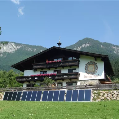 Ein gemütliches, traditionelles Bauernhaus in den Bergen. Solarzellen sind im Vordergrund aufgestellt, um umweltfreundliche Energie zu nutzen.