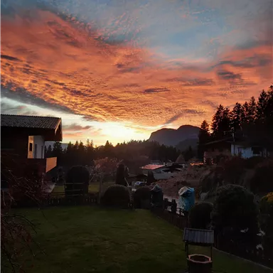 A beautiful sunset with vibrant colors over a picturesque landscape. In the foreground, there is a well-kept garden and houses in the background.