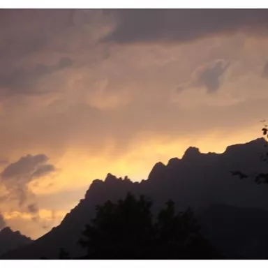 Eine beeindruckende Bergsilhouette vor einem bunten Sonnenuntergang. Der Himmel ist in warmen Farben wie Orange und Gelb gefärbt.