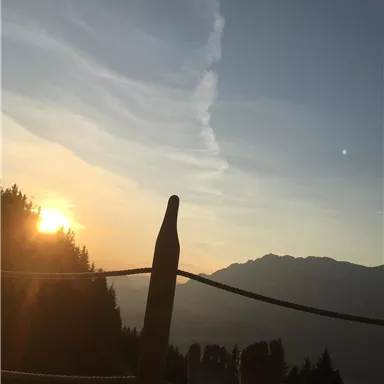 A sunset over the mountains with a view of a clear sky. In the foreground, feet can be seen resting relaxed on a terrace.