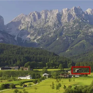 Eine malerische Berglandschaft mit hohen Bergen im Hintergrund und weiten, grünen Wiesen im Vordergrund. Kleine Bauernhöfe sind in der sanften Landschaft verteilt.