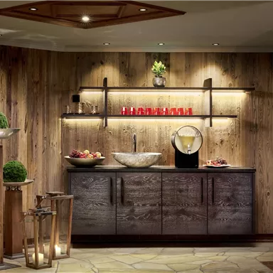 An elegant room with wooden paneling and soft lighting. In the center stands a modern sink with decorations and fruit.