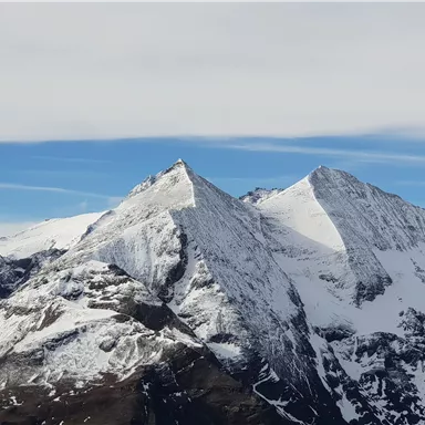 A majestic mountain panorama with snow-covered peaks. The sky is clear and blue, highlighting the beauty of nature.