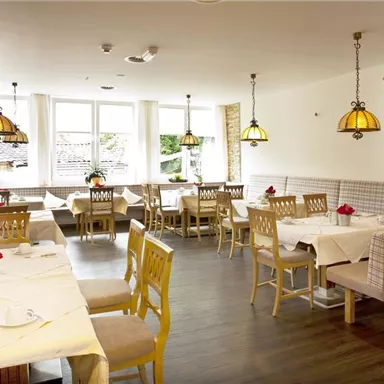 A bright restaurant with elegant wooden chairs and tables. The warm lamps create a cozy atmosphere.