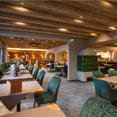 Ein modernes Restaurant mit gemütlicher Atmosphäre und Holzdecke. Die Tische sind stilvoll gedeckt und die Einrichtung ist in sanften Grüntönen gehalten.