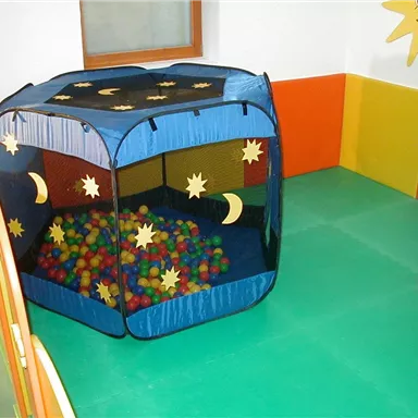 Ein Spielzelt mit bunten Bällen in einem farbenfrohen Spielzimmer. Die Wände sind in leuchtenden Farben gestaltet und es gibt eine große Fensterfläche.