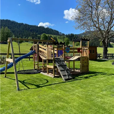 Ein schöner Spielplatz mit Rutschen, Schaukeln und Klettergerüsten. Die grüne Wiese und der blaue Himmel schaffen eine einladende Atmosphäre.