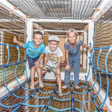 Three children are playing in a climbing net. They are having a lot of fun and laughing together.