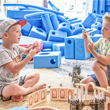 Two little boys are playing with wooden toys on the floor. In the background, colorful building blocks can be seen.