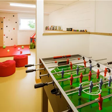 A playroom with a foosball table and climbing walls. Red cushions and colorful play elements create a friendly atmosphere.