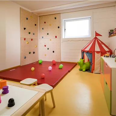 A friendly playroom with a climbing wall and colorful balls. In the corner stands a tent, and the toys are on a table.