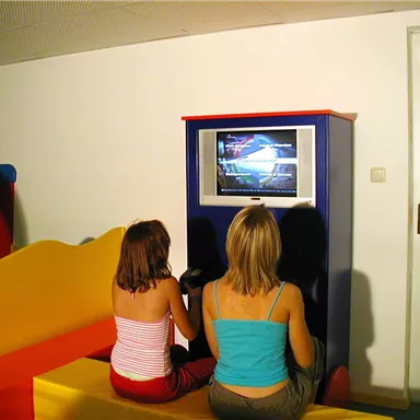 Zwei Mädchen sitzen auf einer bunten Bank und schauen Fernsehen. Der Raum hat ein modernes und einladendes Design.