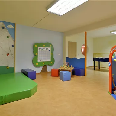 A colorful playroom for children with a climbing wall, soft play blocks, and a play area. The room is brightly and invitingly designed.