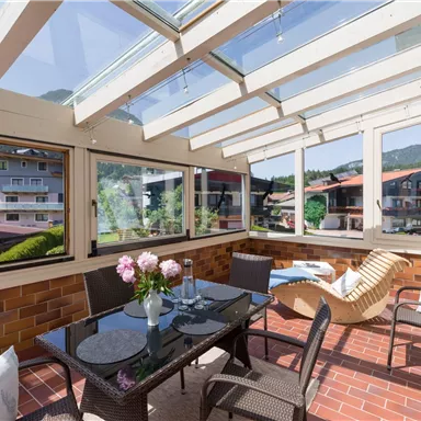 A bright conservatory with large windows and a view of the surroundings. The room is decorated with modern furniture and a table, ideal for relaxing.
