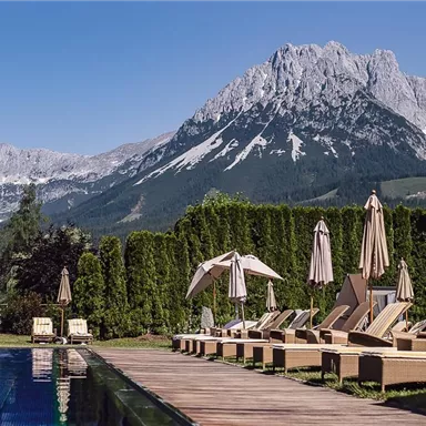 A beautiful outdoor area with a pool and loungers. Majestic mountains can be seen in the background.