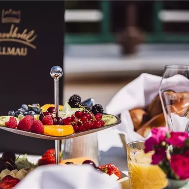 A table with a selection of fresh fruit, including berries and pineapple. Next to it are glasses and a blooming plant.