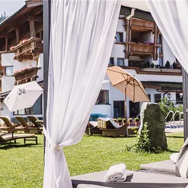 A beautiful view of a hotel with loungers and sunshades in the garden. In the background, gentle hills and trees can be seen.