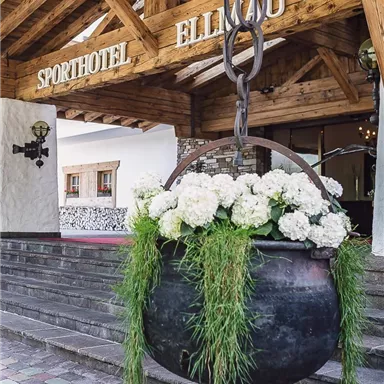 A rustic hotel with an inviting entrance. A large flower bowl with white flowers and green grass hangs above the steps.