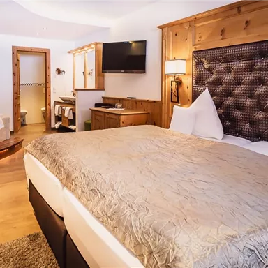 An elegant hotel room with a large bed and wooden interior. In the background, a bathroom and a television are visible.