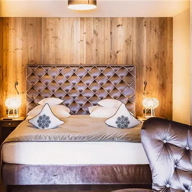 A cozy bedroom with a large, padded bed and an elegant armchair. The walls are made of wood, creating a warm atmosphere.