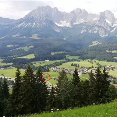 Eine beeindruckende Berglandschaft mit hohen Gipfeln und sanften Wiesen. Im Vordergrund stehen grüne Bäume, die die Aussicht auf das Tal umrahmen.