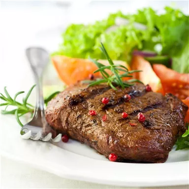 Ein saftiges Steak mit frischen Kräutern und buntem Salat. Das Gericht ist ansprechend angerichtet und röstig, ideal für Feinschmecker.