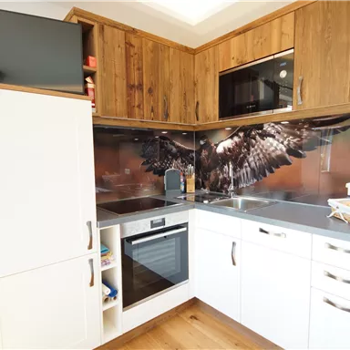 Eine moderne Küche mit Holzoberflächen und grauen Arbeitsplatten. Im Hintergrund ist ein beeindruckendes Wanddesign mit einem Adler zu sehen.