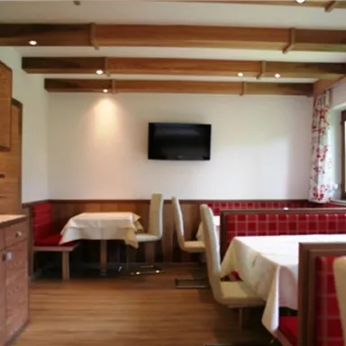 Ein gemütlicher Speiseraum mit Holzvertäfelung und roten Bänken. Ein Fernseher hängt an der Wand und große Fenster lassen viel Licht herein.