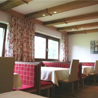 Ein gemütliches Restaurant mit roten Sitzbänken und hellen Tischdecken. Große Fenster sorgen für viel Tageslicht.