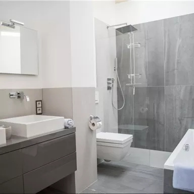 Ein modernes Badezimmer mit einer eleganten Dusche und einer Badewanne. Es verfügt über zwei Waschbecken und stilvolle graue Fliesen.